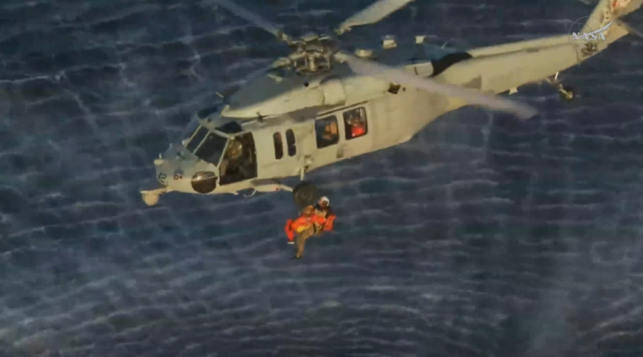 Artemis II Commander and NASA astronaut Reid Wiseman is being hoisted into a U.S. military helicopter before being transported to the USS John P. Murtha.